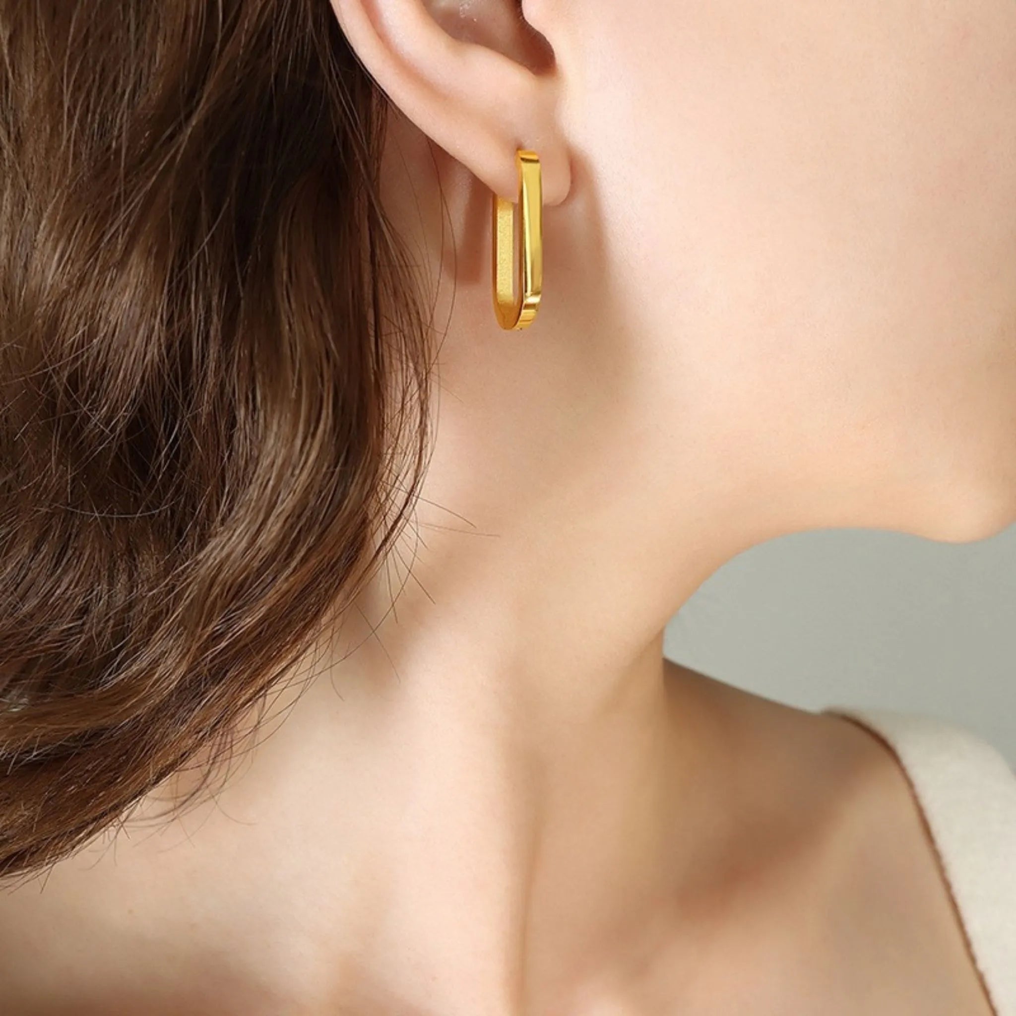 Frau mit glattem Haar trägt einen ovalen goldenen Creolenohrring mit schlichtem Design am Ohr
