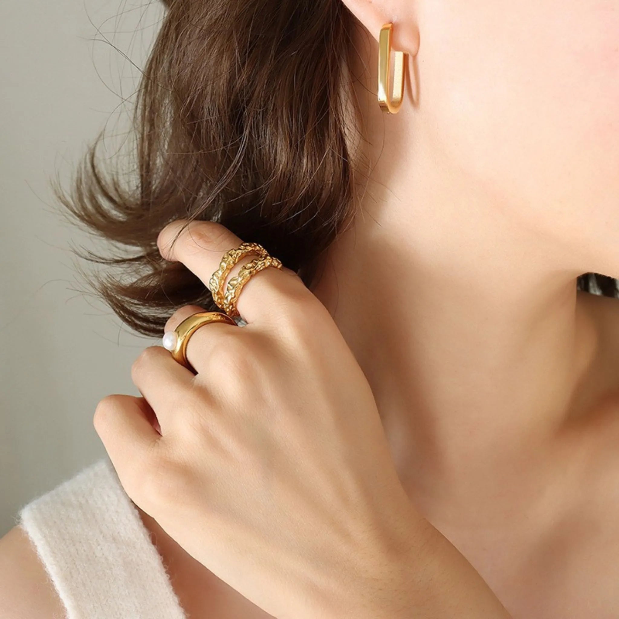 Frau mit glattem Haar trägt einen ovalen goldenen Creolenohrring mit schlichtem Design am Ohr