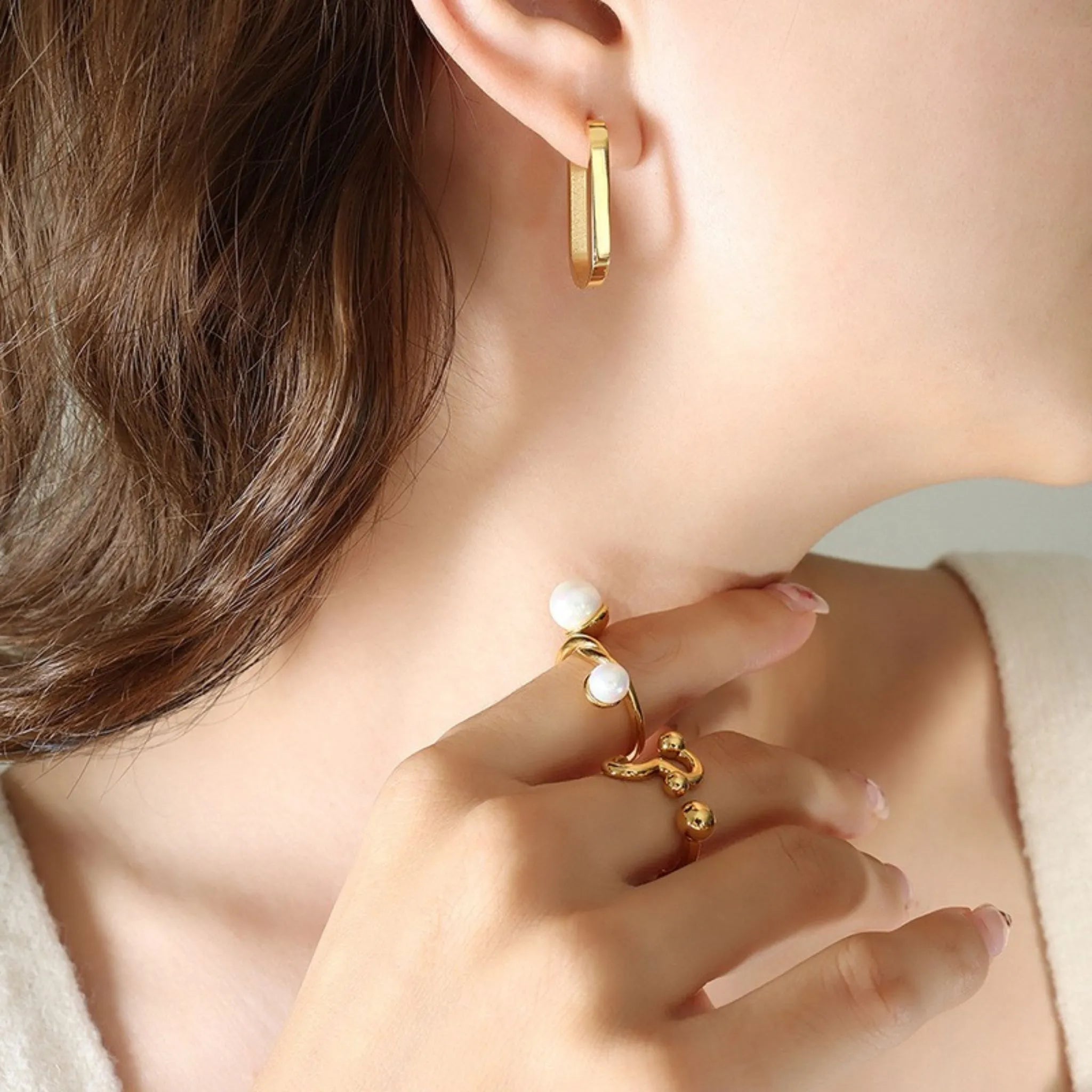 Frau mit glattem Haar trägt einen ovalen goldenen Creolenohrring mit schlichtem Design am Ohr