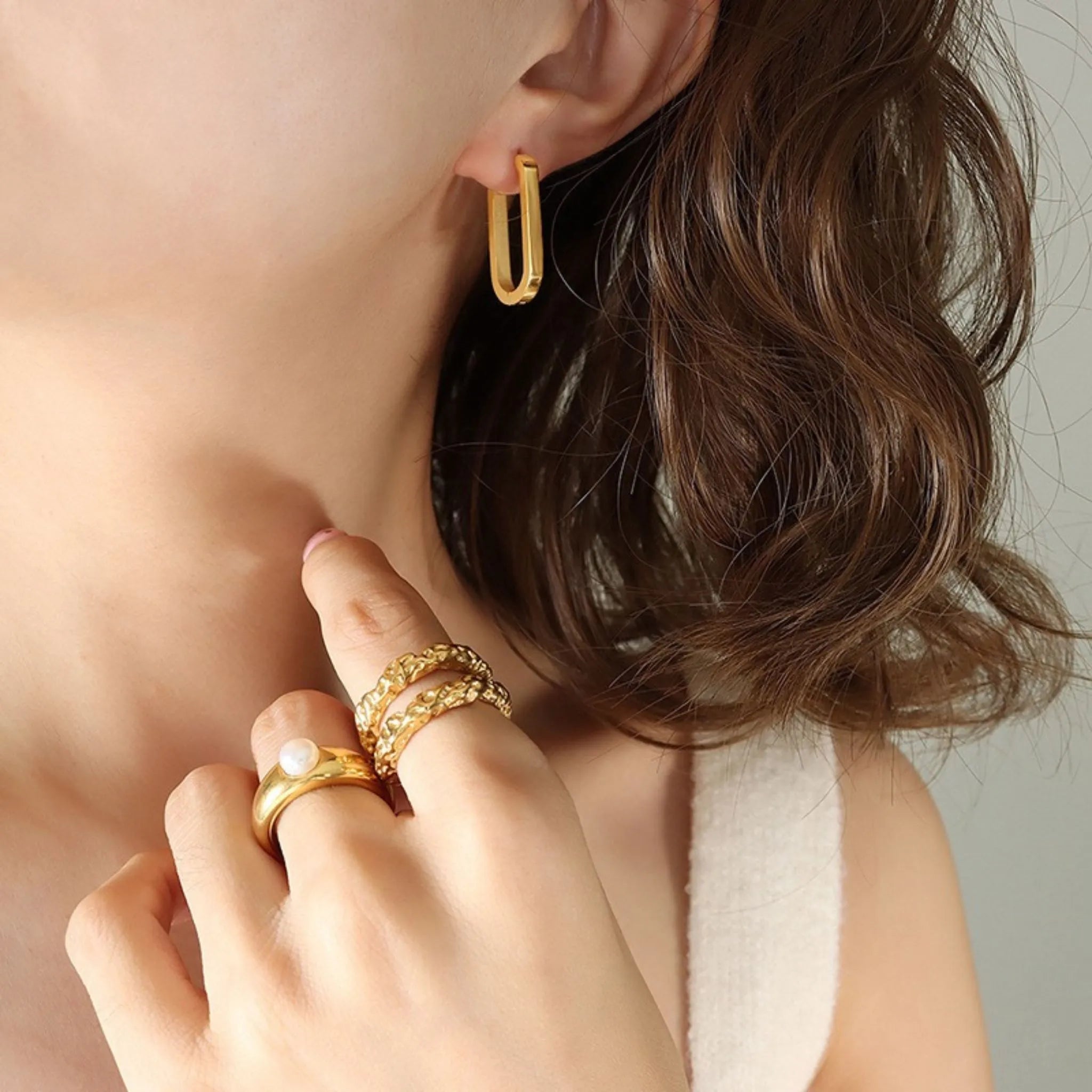 Frau mit glattem Haar trägt einen ovalen goldenen Creolenohrring mit schlichtem Design am Ohr